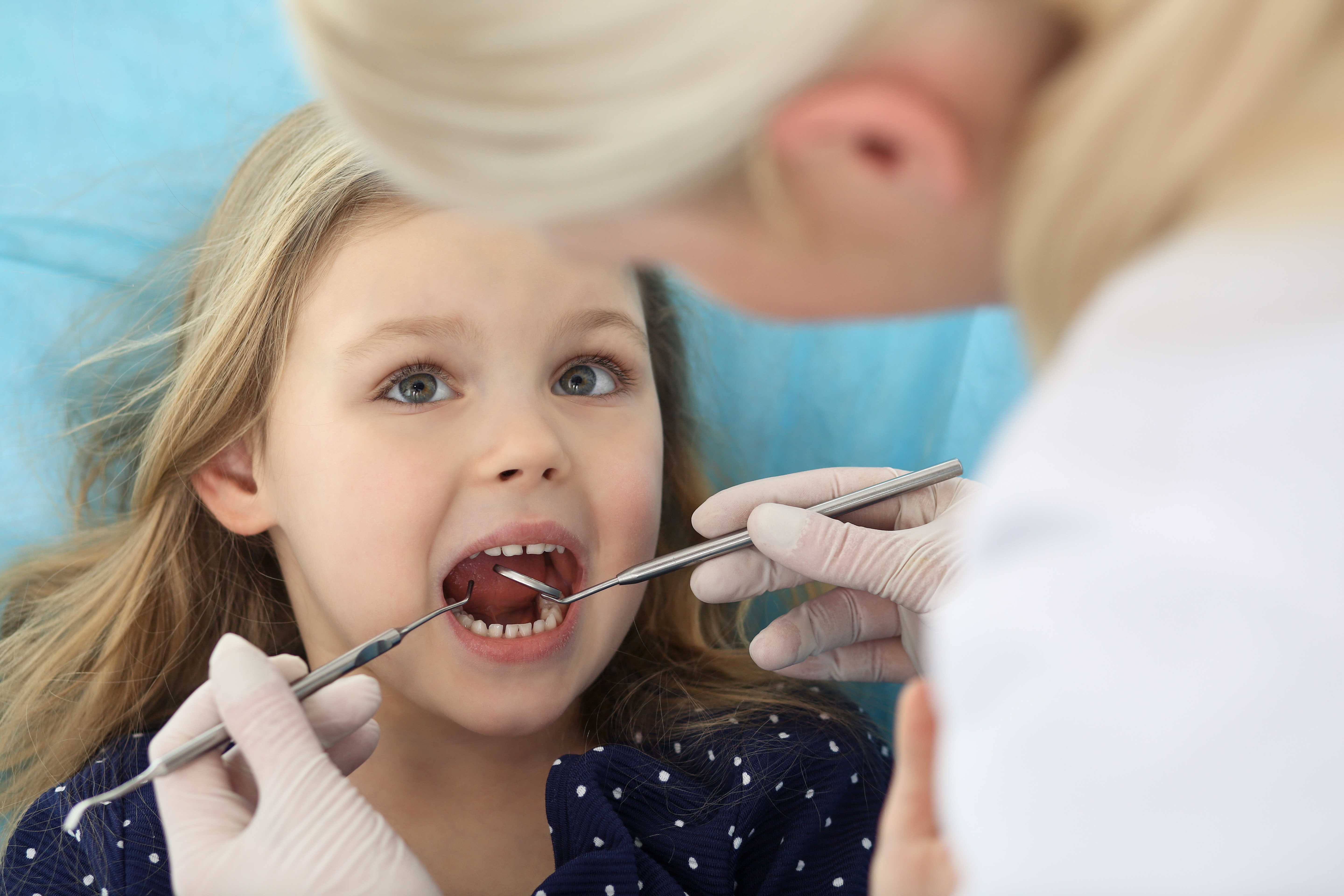 Little baby girl sitting at dental chair with open mouth and feeling fear during oral check up while doctor. Visiting dentist office. Medicine concept